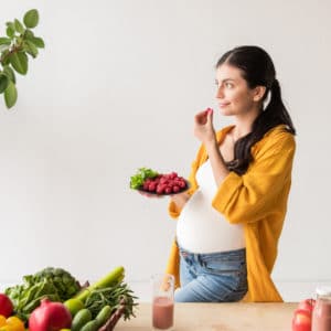 Una giovane donna incinta mangia della frutta fresca in cucina.