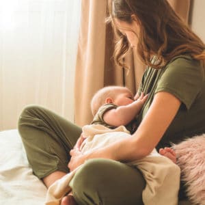 Una giovane madre allatta il figlio neonato al seno, seduta sul letto in camera.