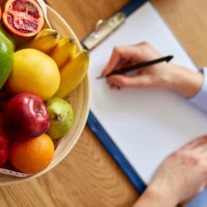 Una donna inizia a scrivere su un blocco per appunti. Sullo stesso tavolo è presente anche una cesta di frutta fresca.