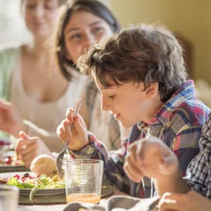 Un ragazzo di circa 12 anni mangia insieme ad altre persone.